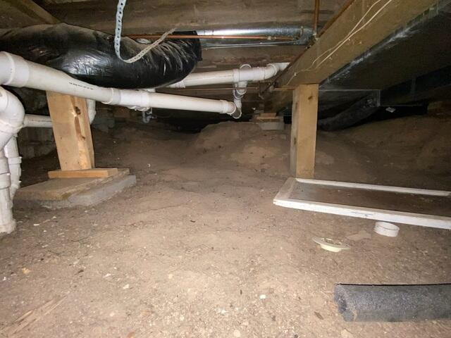 Unconditioned open dirt crawl space floor showing exposed pipes and dark framing before repair near Spooner Wisconsin