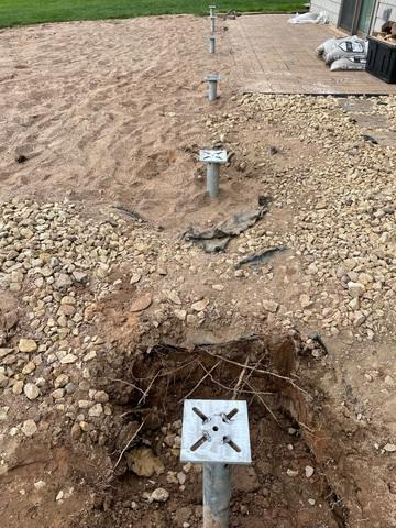 deck-foundation-stabilization-helical-piers-shell-lake-wi A row of heavy-duty steel helical pier brackets and galvanized shafts installed deep inside excavated ground trenches in a yard in Shell Lake, WI.