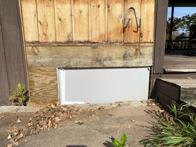 An exterior view of a home's lower wooden siding featuring a newly installed gray crawl space access panel and unpainted wood skirting panels in Jim Falls, WI.