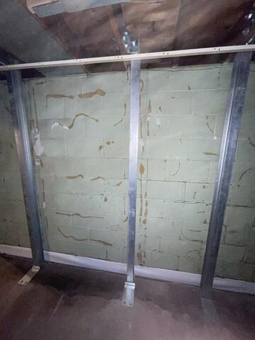 A long concrete block basement wall showing severe horizontal cracking and extensive moisture peeling across the block joints in Esko, MN before repair.