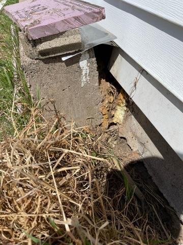 A shifted exterior concrete block foundation pier and exposed deteriorating pink insulation board beneath vinyl siding on a home in Clayton, WI before repair.