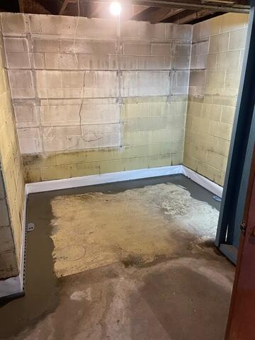 A small basement utility room corner showing a freshly poured concrete perimeter trench covering a sub-floor drainage track beneath clean block walls in Esko, MN.