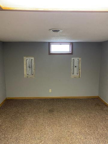 An immaculate view of a finished basement room with grey walls and brown carpet in Shell Lake, WI, showing two heavy-duty steel Geo-Lock wall anchor plates neatly installed inside drywall cutouts below a small window.