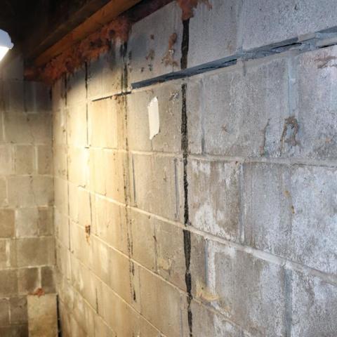Severe vertical and stair-step cracks in a painted basement wall