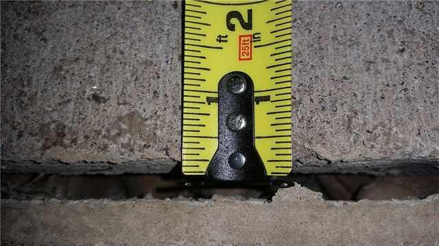 A close-up view of a yellow tape measure calculating a prominent horizontal crack displacement in a concrete block foundation wall in Wrenshall, MN.