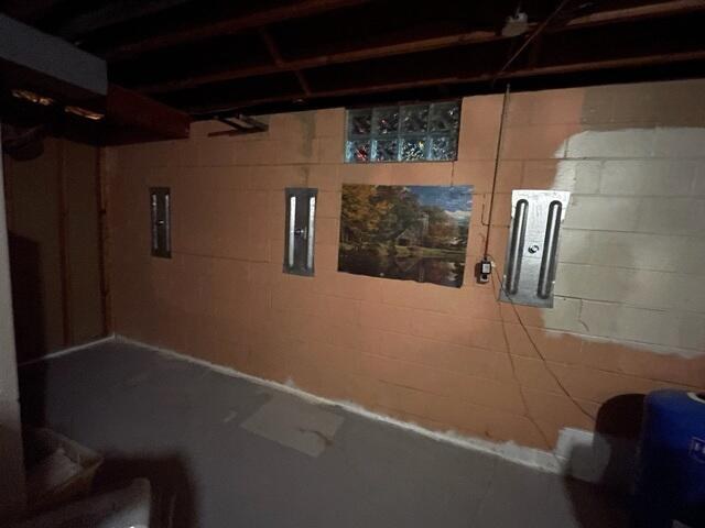 An interior basement view in Washburn, WI showing three galvanized steel GeoLock wall anchor plates mounted on an orange-painted block foundation wall.