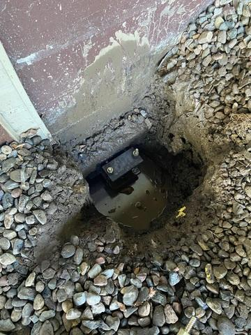 A close-up look inside an excavated foundation pit showing a heavy black steel push pier bracket mounted tightly against a concrete footing in Palisade, MN.