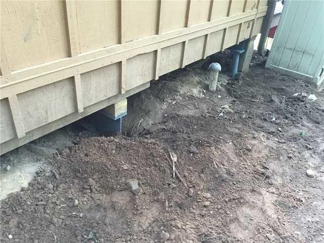 Excavation site along the exterior timber siding of a sinking cabin during the installation of steel support beams and HelixPro helical piers in Sarona Wisconsin