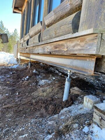 A newly installed heavy steel horizontal I-beam supported by industrial galvanized steel helical piers driven into the ground under a log cabin in Holyoke, MN.