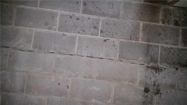 A concrete block basement foundation wall in Wrenshall, MN showing a severe horizontal crack along a mortar joint accompanied by dark water stains.
