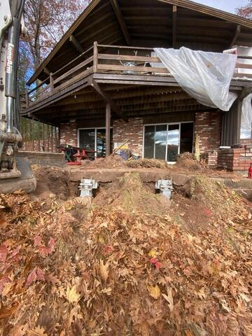 An exterior view of a brick home features two newly installed high-capacity steel foundation push pier brackets supporting a concrete recreation slab edge in Iron River, WI.