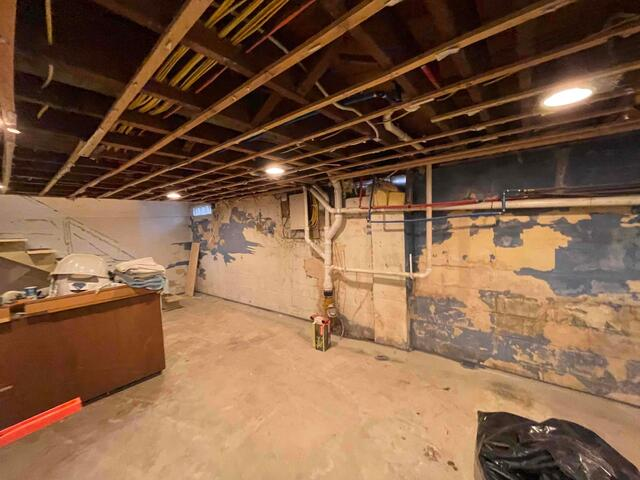 A large residential basement in Remer, MN featuring exposed overhead wood framing and peeling blue paint along concrete block walls before repair.