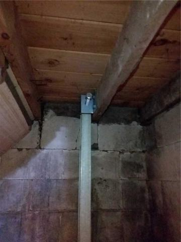 An interior basement view in Almena, WI, showing a heavy-duty vertical steel PowerBrace support beam cleanly mounted to an adjustable bracket against an old concrete block wall beneath wooden floor joists.