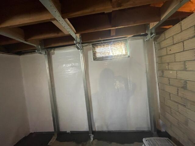 A close-up view of two vertical steel PowerBrace I-beam support columns mounted against a white-covered foundation wall near a basement window in Eau Claire, WI.