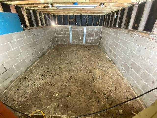 A wide view of an open dirt basement showing two vertical steel PowerBrace support columns installed against a concrete block foundation wall in McGregor, MN.