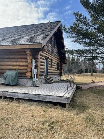 rustic-log-home-exterior-deck-holyoke-mn An exterior view of a rustic log lodge featuring a wide wooden plank deck and concrete block perimeter foundation in Holyoke, MN.