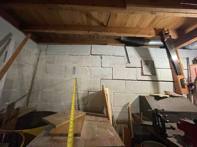 A close-up view of a cracked and bowing concrete block basement wall being measured with a yellow tape measure in Danbury, WI before repair.