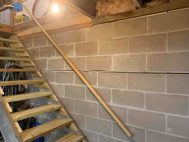 A severe horizontal crack splitting a concrete block basement foundation wall behind a wooden staircase handrail in Comstock, WI before repair.