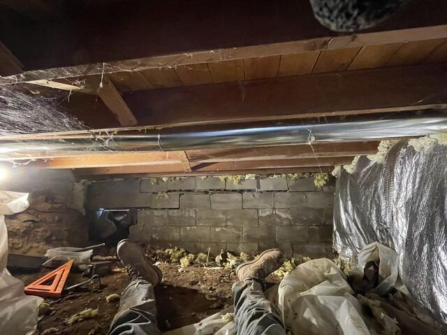 A view inside a low-clearance crawl space showing a severely cracked and inward-bowing concrete block foundation wall in Frederic, WI before repair.
