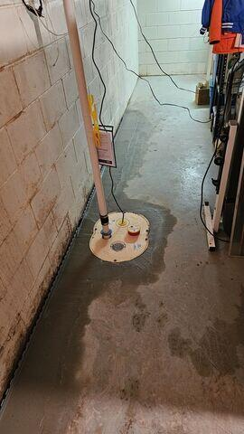 A newly installed SingleSafe sump pump system with its basin cover neatly sealed into a fresh concrete floor perimeter trench along a block wall in Stone Lake, WI.