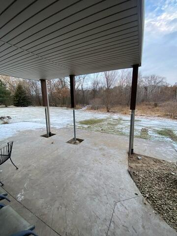 A wide exterior view of a two-story residential home featuring an elevated room addition supported by timber columns over a concrete patio in Andover, MN.