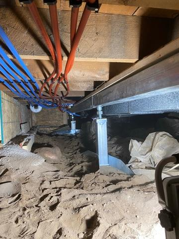 An immaculate crawl space view in Dresser, WI showing a heavy-duty steel SmartJack support system cleanly reinforcing floor beams next to red and blue PEX plumbing supply lines.