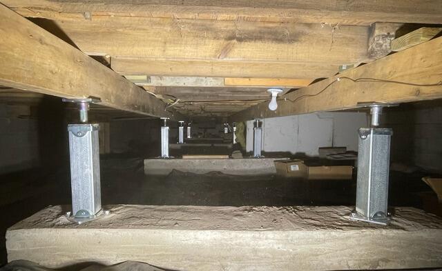 An immaculate view inside a completed crawl space project in Luck, WI, showing a uniform row of heavy-duty galvanized steel SmartJack support columns reinforcing wood beams.
