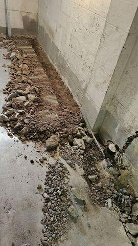 An active basement waterproofing construction zone near Remer, MN, showing a broken concrete and dirt trench excavated along a masonry block wall footing.