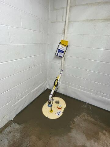 An immaculate view of a newly installed sump pump system surrounded by fresh concrete in a white-painted block basement corner in Grand Marais, MN.