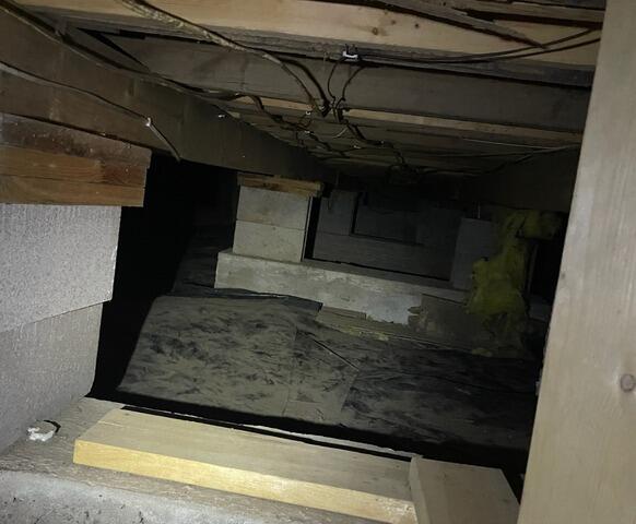 A view inside a dark, unconditioned crawl space showing an exposed dirt floor, concrete block piers, and wooden floor joists in Luck, WI before repair.