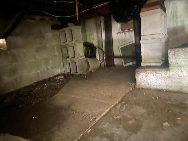 A dark, unreinforced crawl space showing shifting stacks of hollow concrete blocks beneath floor framing beams in Richfield, MN before repair.